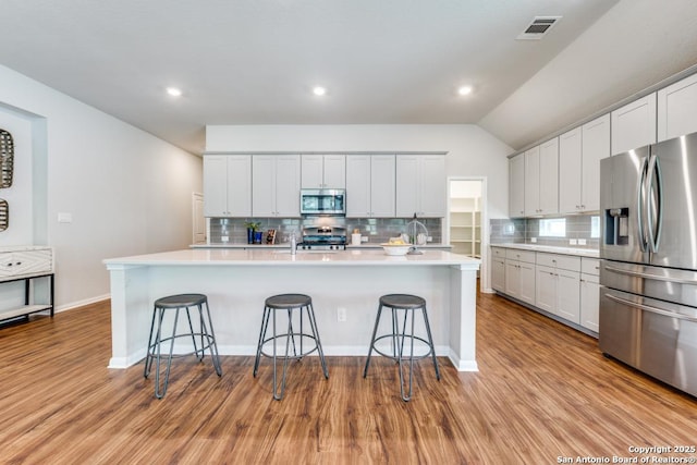 kitchen with a breakfast bar area, stainless steel appliances, visible vents, and tasteful backsplash