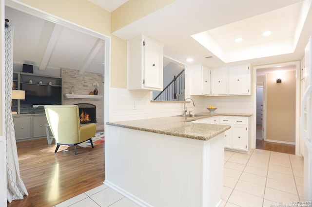 kitchen with a brick fireplace, white cabinetry, light stone counters, and a sink
