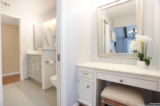 bathroom with visible vents, an inviting chandelier, vanity, toilet, and baseboards