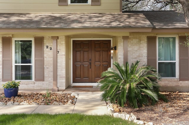 doorway to property featuring roof with shingles and brick siding