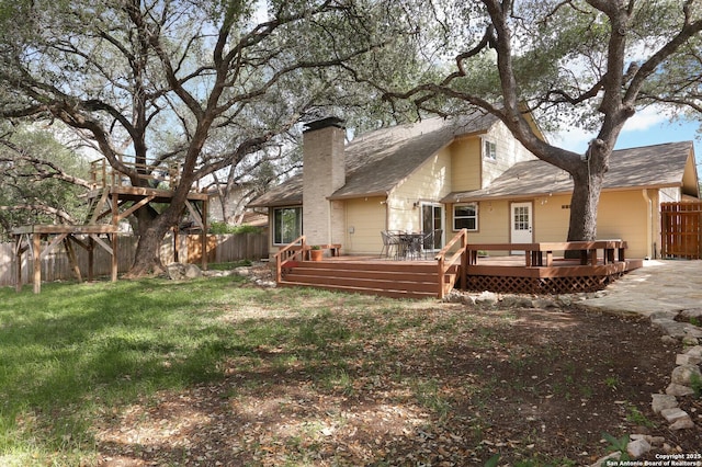 rear view of property with a deck, a fenced backyard, roof with shingles, a chimney, and a yard