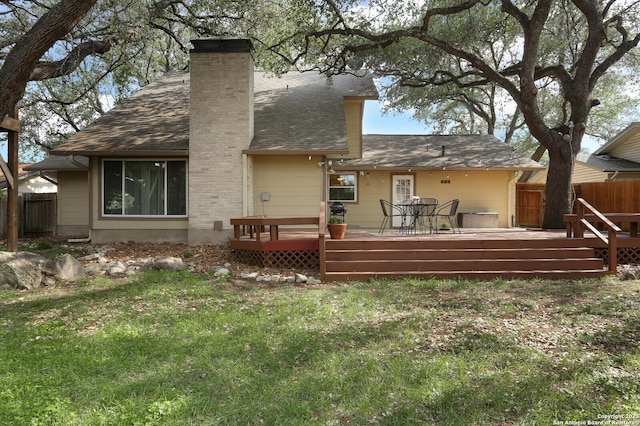 back of property with fence, a wooden deck, a chimney, and a lawn