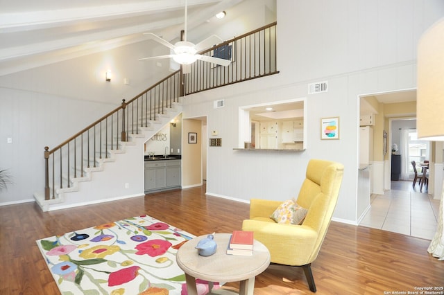 living area featuring stairway, high vaulted ceiling, wood finished floors, and visible vents