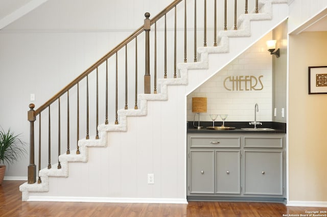 bar with indoor wet bar, a sink, stairs, and wood finished floors