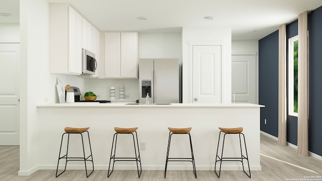 kitchen featuring white cabinets, a breakfast bar, light wood finished floors, stainless steel appliances, and a peninsula