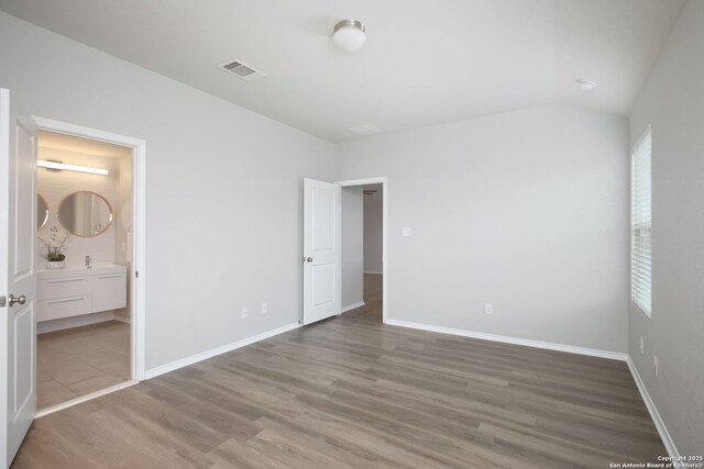 unfurnished bedroom featuring ensuite bath, baseboards, wood finished floors, lofted ceiling, and visible vents