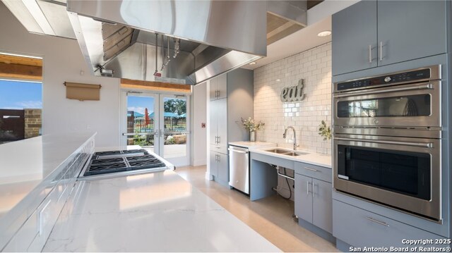 kitchen with light countertops, gray cabinets, a sink, backsplash, and stainless steel appliances