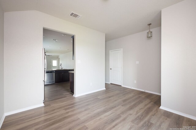 spare room featuring visible vents, a sink, baseboards, and wood finished floors