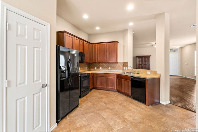 kitchen featuring a sink, light countertops, brown cabinetry, backsplash, and black appliances