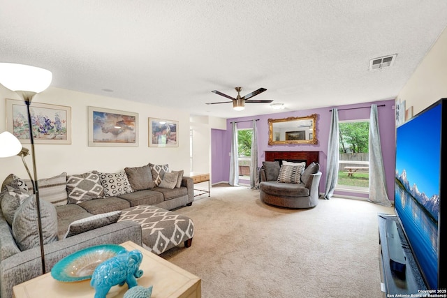carpeted living room with a textured ceiling, visible vents, ceiling fan, and a fireplace