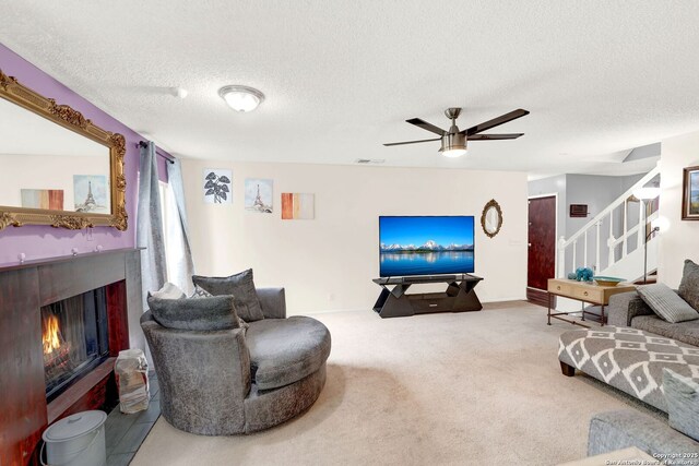 8034 Deadwood Rdg, Converse, TX 78109 - carpeted living room featuring visible vents, stairs, ceiling fan, a warm lit fireplace, and a textured ceiling