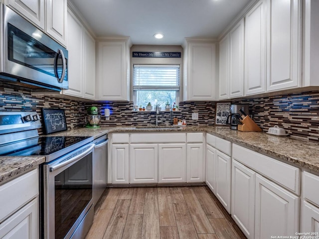 kitchen featuring backsplash, appliances with stainless steel finishes, a sink, light wood-style floors, and white cabinetry
