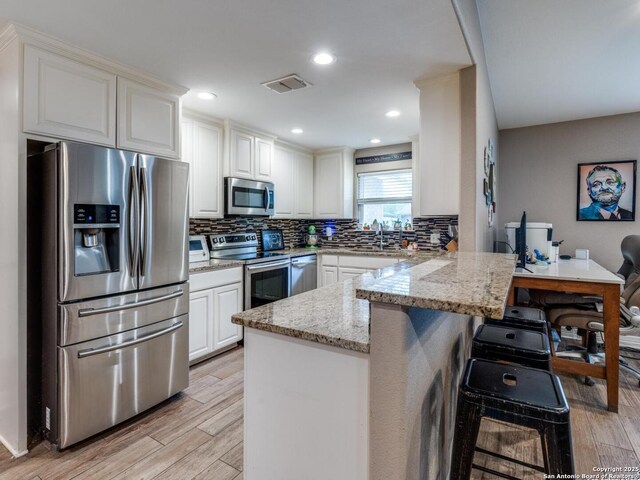 kitchen with light wood-type flooring, a peninsula, a sink, and appliances with stainless steel finishes