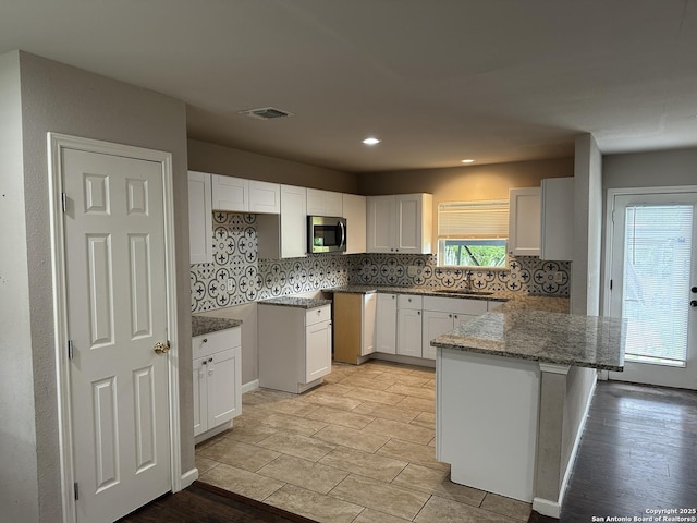 kitchen with a sink, a peninsula, stainless steel microwave, decorative backsplash, and visible vents
