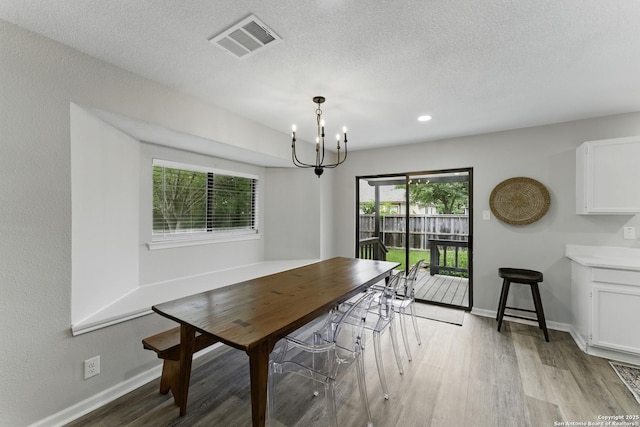 dining room featuring visible vents, baseboards, a textured ceiling, light wood-style flooring, and a notable chandelier
