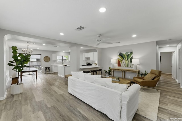 living room featuring visible vents, baseboards, ceiling fan with notable chandelier, light wood finished floors, and recessed lighting