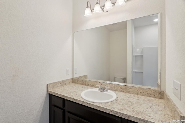 bathroom with toilet, a textured wall, and vanity