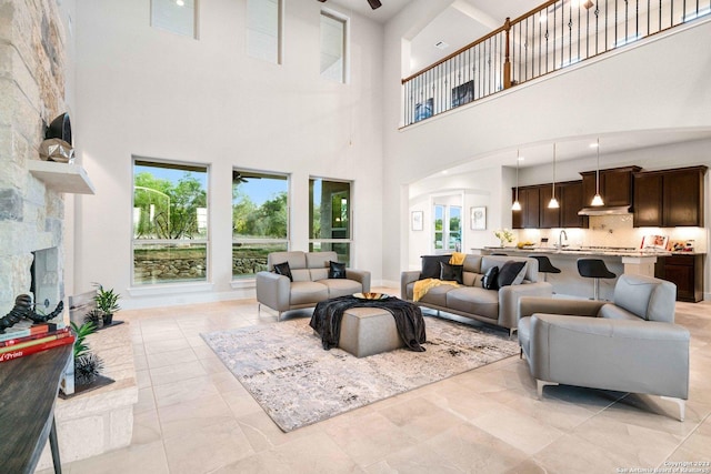 living area with arched walkways, a high ceiling, a ceiling fan, and a stone fireplace