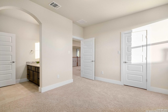 unfurnished bedroom featuring arched walkways, baseboards, visible vents, and light carpet