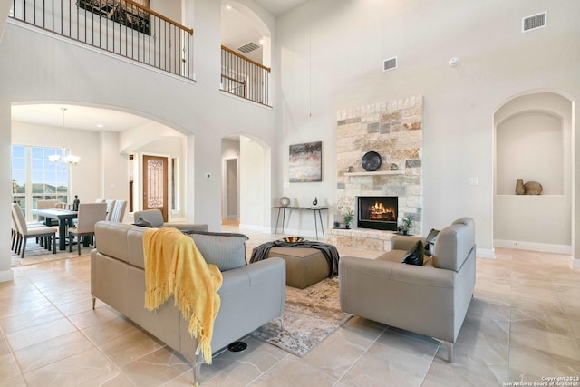 living room featuring visible vents, arched walkways, a fireplace, an inviting chandelier, and a high ceiling
