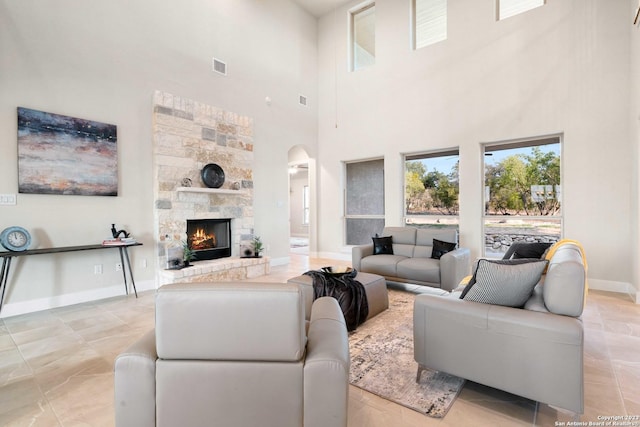 living room with arched walkways, a stone fireplace, baseboards, a towering ceiling, and visible vents