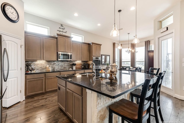 kitchen with decorative backsplash, a kitchen island with sink, a kitchen breakfast bar, a sink, and stainless steel appliances
