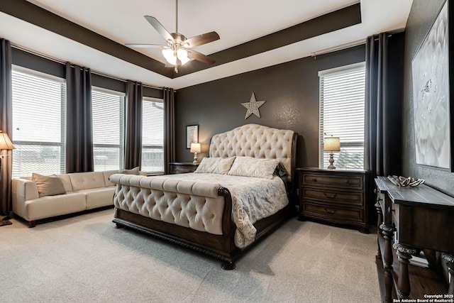 bedroom with a raised ceiling, light carpet, and a ceiling fan