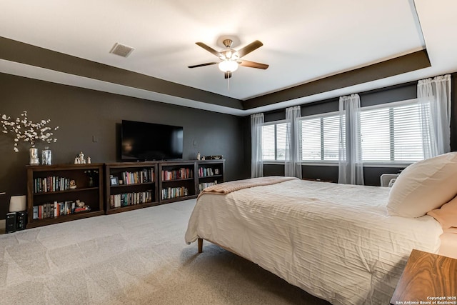 carpeted bedroom featuring ceiling fan, a tray ceiling, and visible vents