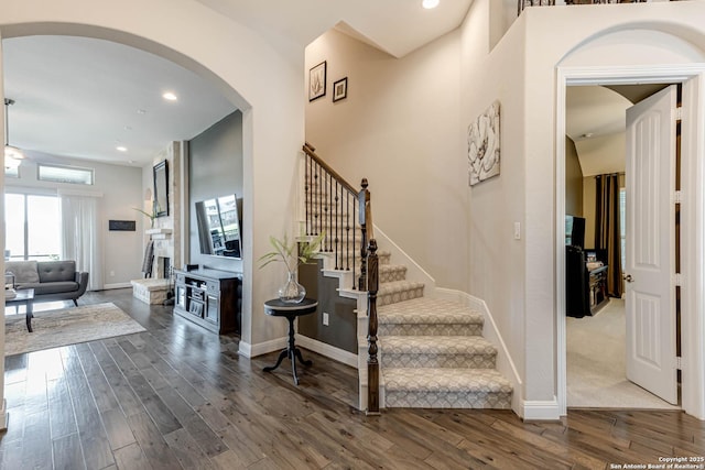 stairway featuring baseboards, arched walkways, wood finished floors, and recessed lighting