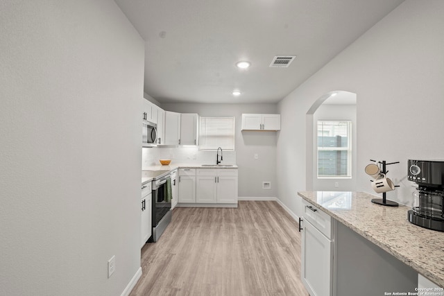 kitchen with appliances with stainless steel finishes, a sink, arched walkways, light wood-type flooring, and visible vents
