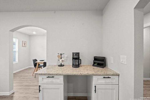 kitchen featuring arched walkways, baseboards, white cabinets, light stone counters, and light wood-style floors