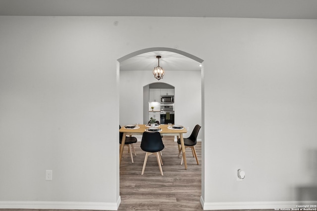 dining area with arched walkways, baseboards, and wood finished floors