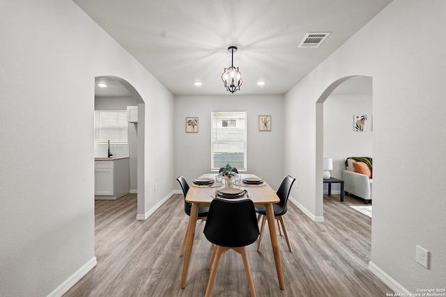 dining space featuring arched walkways, baseboards, light wood-type flooring, and visible vents