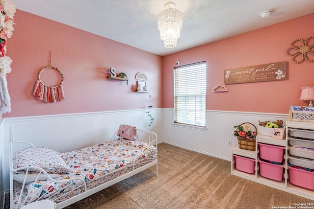 carpeted bedroom featuring a notable chandelier and a wainscoted wall