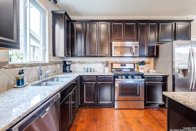 kitchen with appliances with stainless steel finishes, a healthy amount of sunlight, a sink, and light stone counters