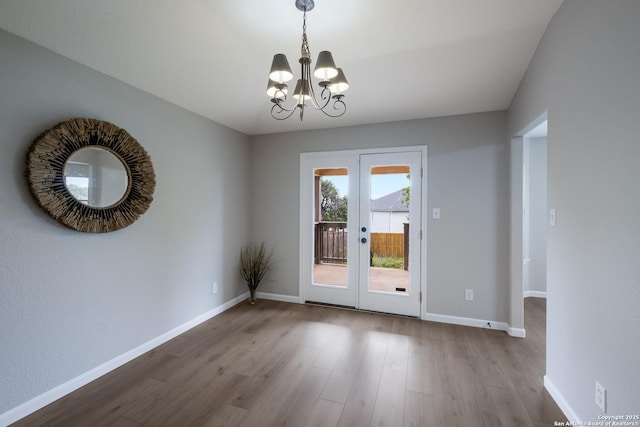 unfurnished dining area featuring french doors, baseboards, wood finished floors, and an inviting chandelier