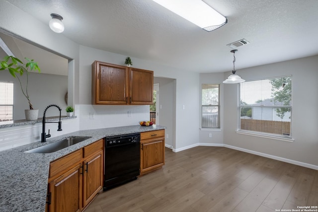 kitchen with visible vents, brown cabinetry, black dishwasher, light wood-type flooring, and a sink