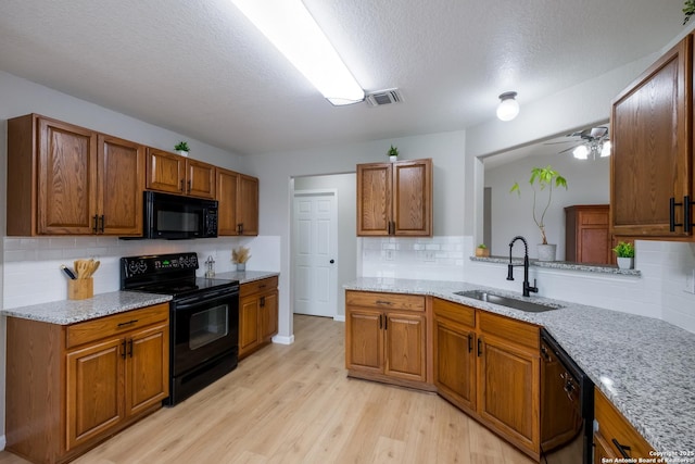 kitchen featuring brown cabinetry, light wood-style floors, a sink, backsplash, and black appliances