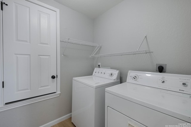 clothes washing area with laundry area, washing machine and dryer, baseboards, and light wood-style floors
