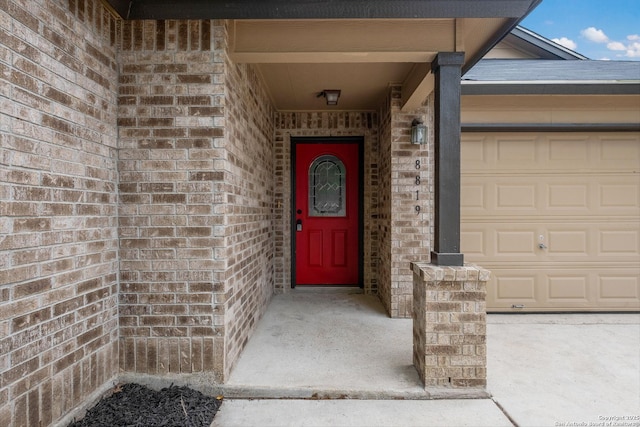 view of exterior entry with brick siding and a garage