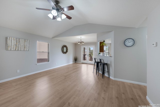 living area featuring baseboards, vaulted ceiling, light wood finished floors, and ceiling fan with notable chandelier