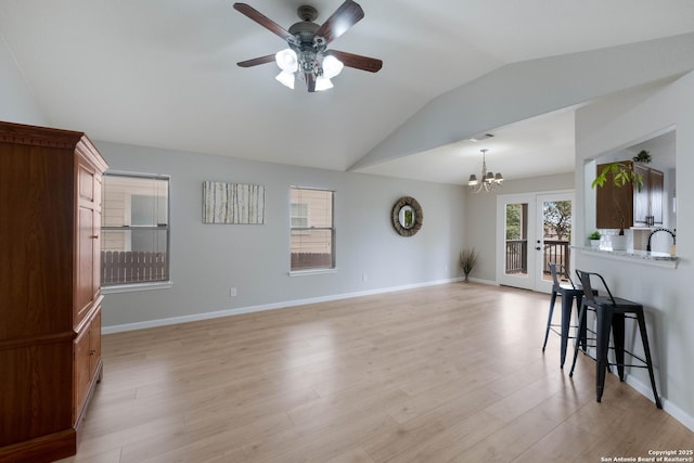 living area with baseboards, light wood finished floors, ceiling fan with notable chandelier, and lofted ceiling