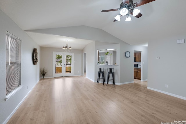unfurnished living room featuring baseboards, light wood finished floors, lofted ceiling, and ceiling fan with notable chandelier