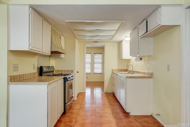 kitchen with exhaust hood, stainless steel range with gas stovetop, a sink, light tile patterned floors, and light countertops