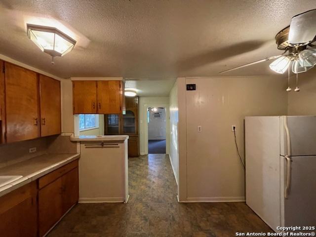kitchen featuring a ceiling fan, a textured ceiling, brown cabinets, freestanding refrigerator, and a peninsula