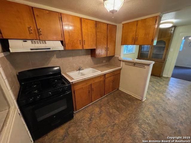 kitchen featuring under cabinet range hood, black range with gas cooktop, brown cabinetry, and a sink