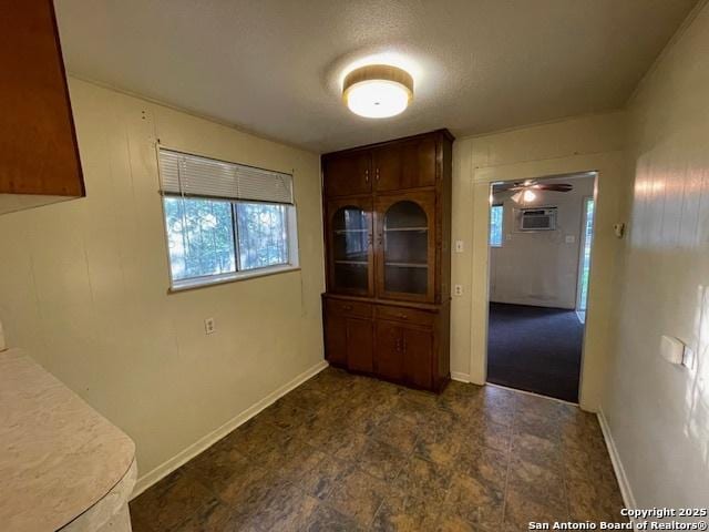 unfurnished dining area featuring a ceiling fan, baseboards, and a wall unit AC