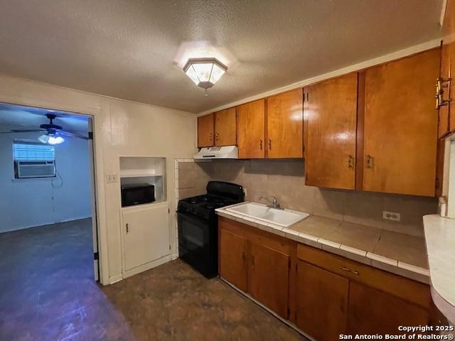 kitchen with brown cabinets, exhaust hood, a sink, gas stove, and tile countertops