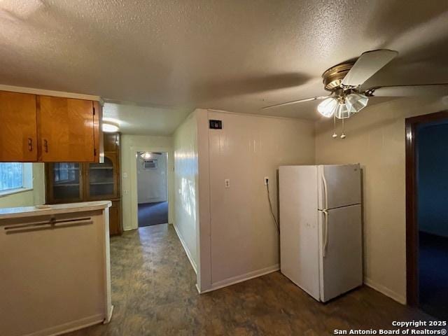 kitchen featuring brown cabinetry, freestanding refrigerator, baseboards, ceiling fan, and a textured ceiling