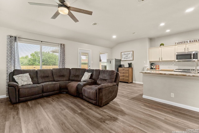 living room with plenty of natural light, a ceiling fan, light wood-style flooring, and baseboards